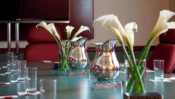 A conference table with vases of white flowers, clear glasses, and a power strip.