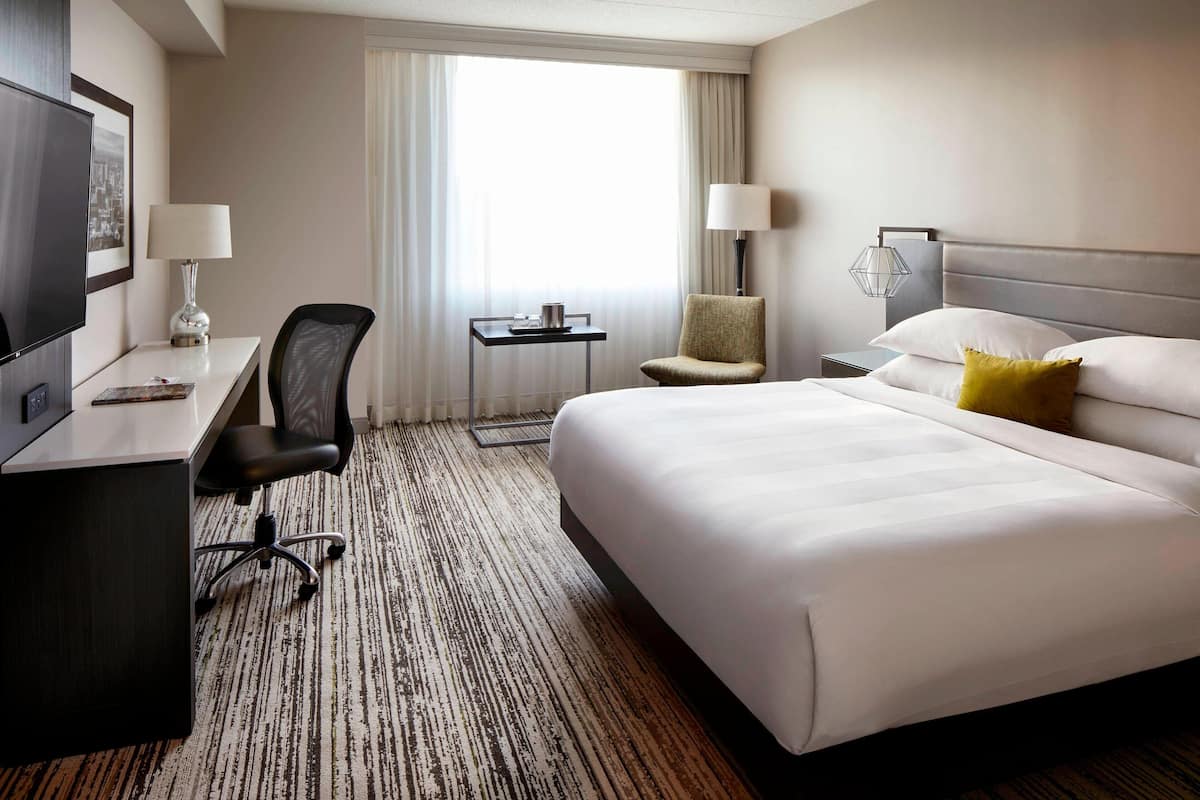 Una habitación de hotel con una cama grande, un escritorio, una silla, un televisor y una ventana con cortinas.