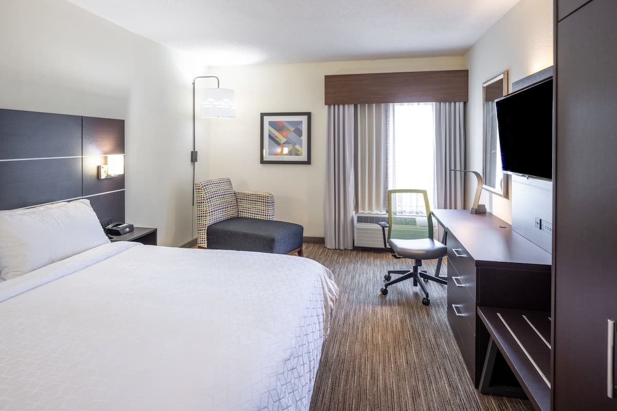 A hotel room with a large bed, a desk with a chair, a TV, and a window with curtains.