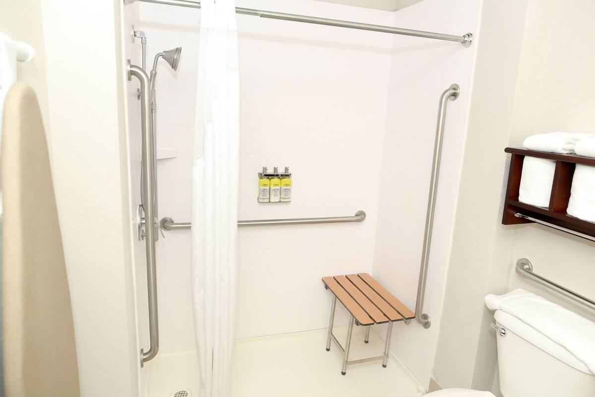 A bathroom with a shower, toilet, and a small wooden bench.