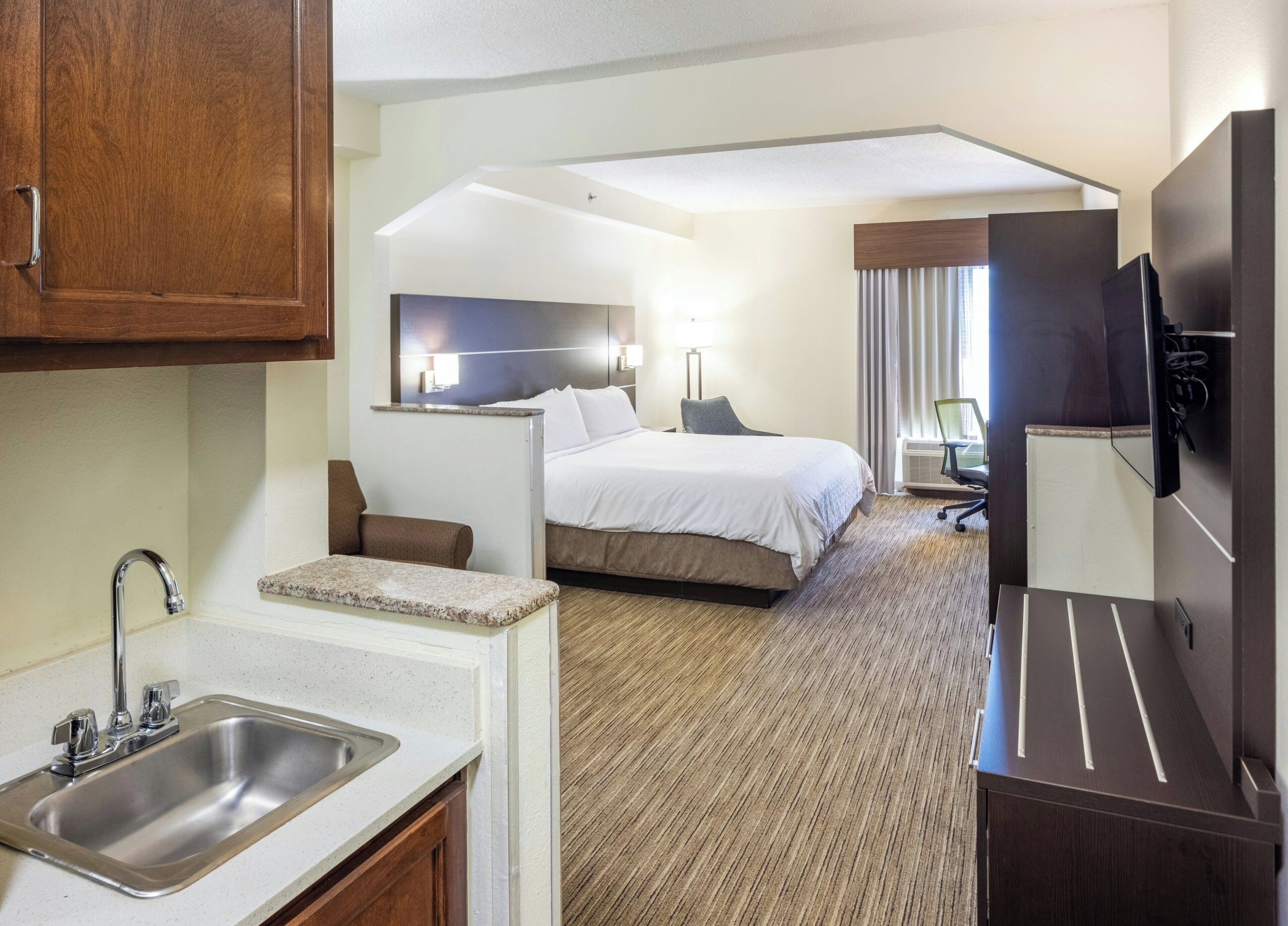 Une chambre d’hôtel équipée d’un lit, d’un bureau, d’une télévision, d’un lavabo et d’un miroir.