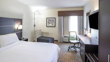 A hotel room with a large bed, a desk with a chair, a flat-screen TV, and a window with curtains.