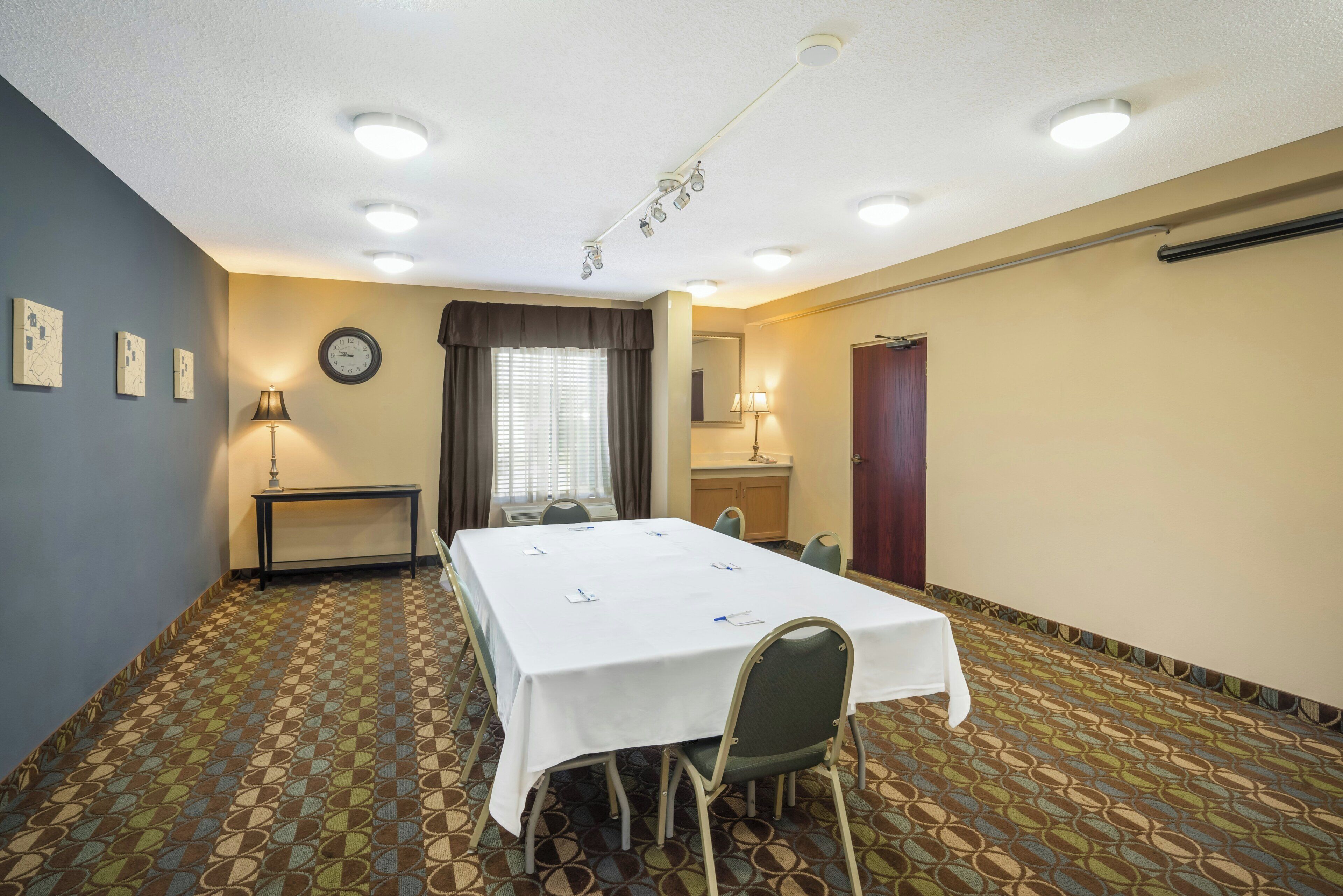 A conference room with a long table, chairs, a clock, and a window with curtains.