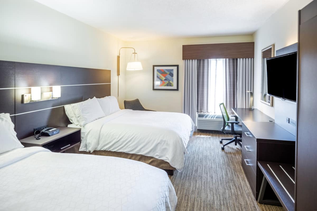 A hotel room with two beds, a desk, a television, and a window with curtains.