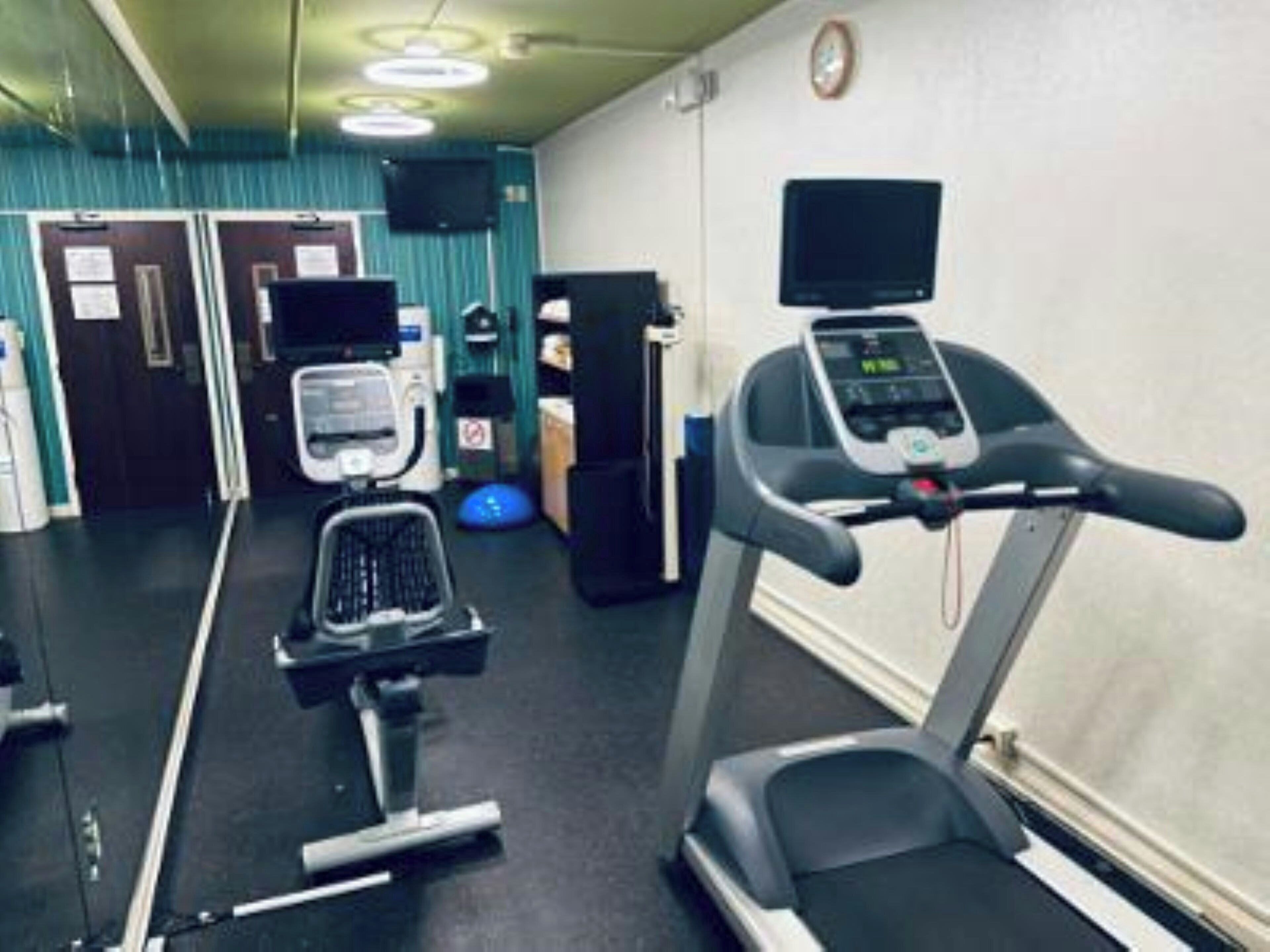 Une salle de sport équipée de matériel d’exercice, notamment un tapis de course et un vélo d’appartement.