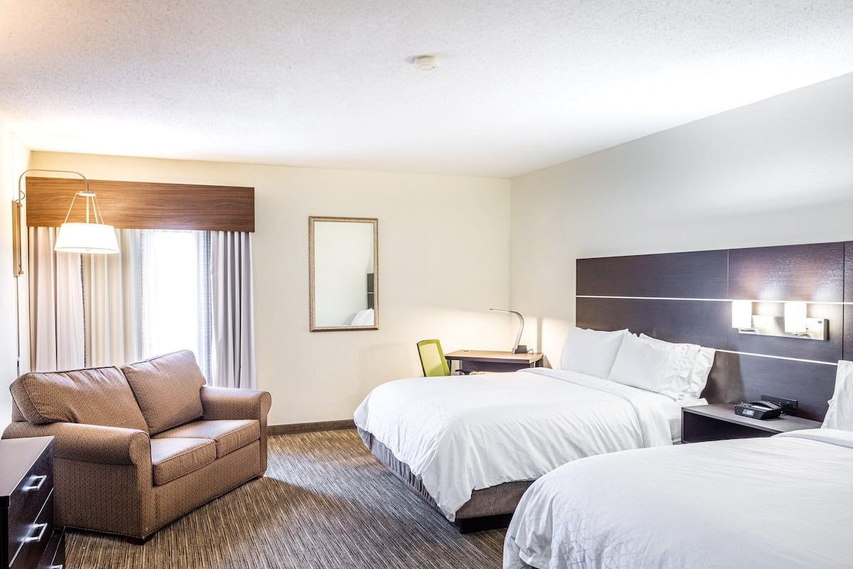 A hotel room with two beds, a sofa, a desk, and a chair.