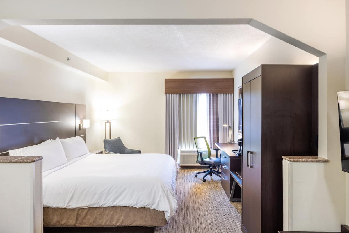 A hotel room with a large bed, a desk, a chair, and a wardrobe.