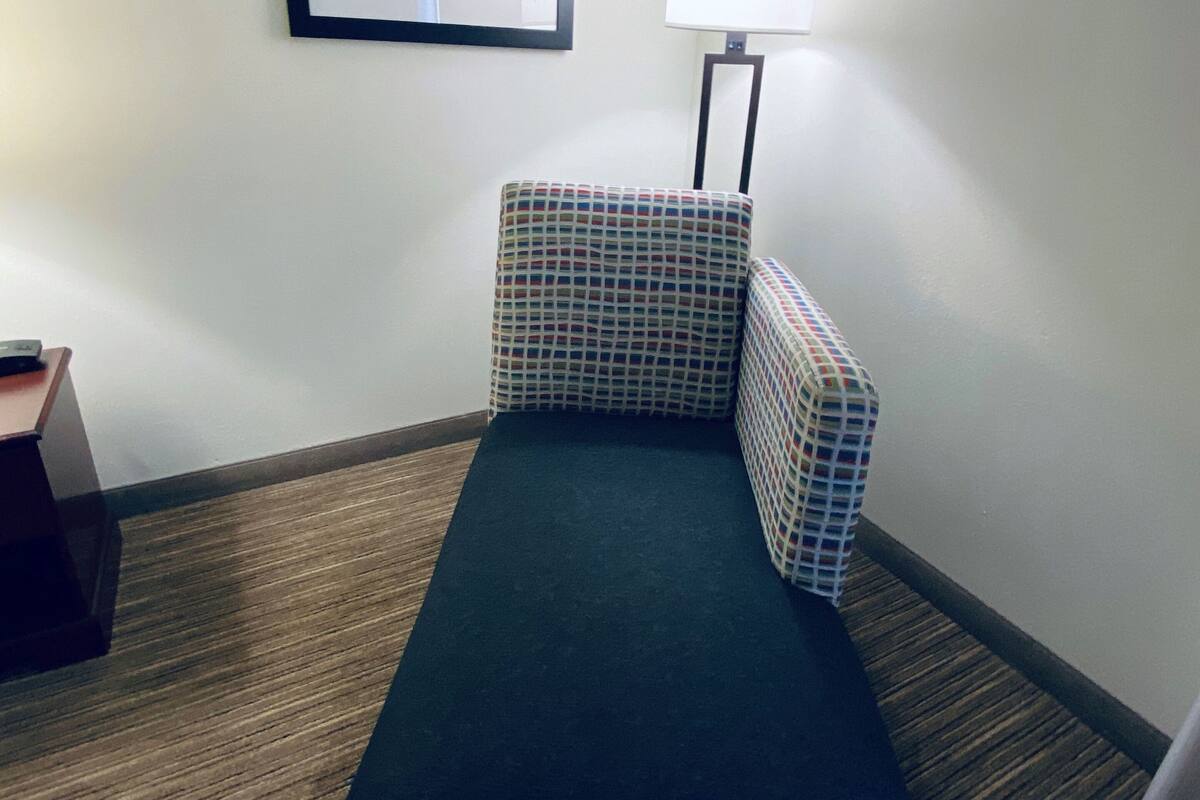 A small, dark-colored sofa with a checkered pattern, a framed abstract painting on the wall, and a floor lamp.