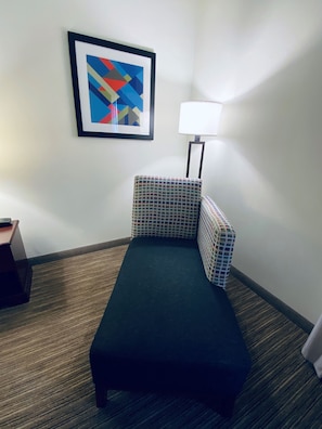 A small, dark-colored sofa with a checkered pattern, a framed abstract painting on the wall, and a floor lamp.