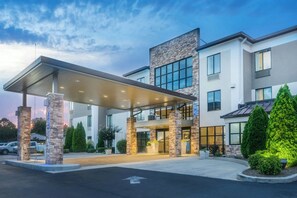 A modern hotel with a covered entrance, stone pillars, and a landscaped driveway.