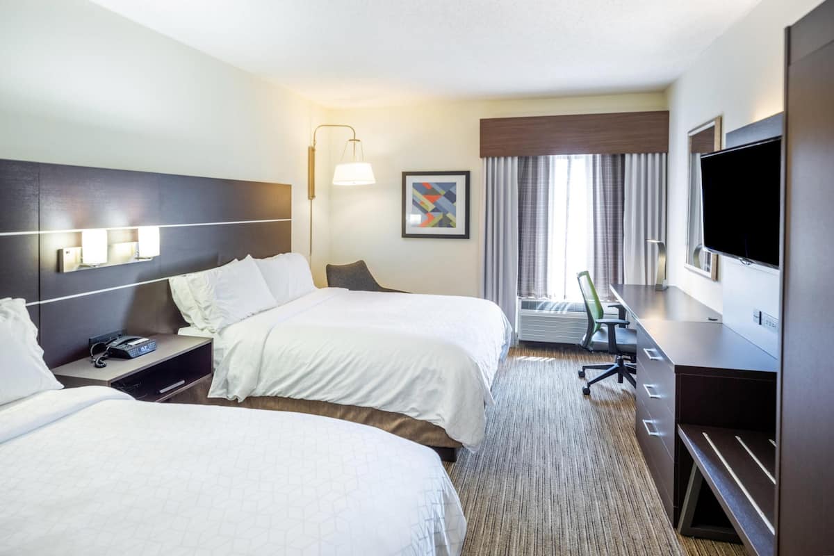 A hotel room with two beds, a desk, a television, and a window with curtains.