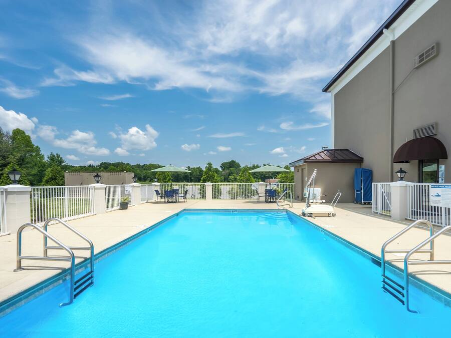 A rectangular swimming pool with a clear blue water surface, surrounded by a white fence, and a building with a brown roof to the right.