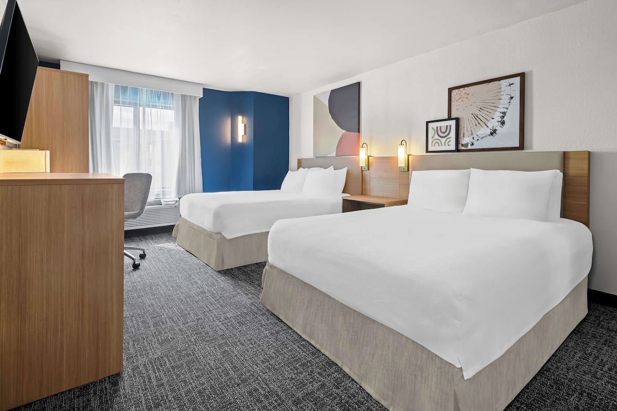 A hotel room with two beds, a desk, a chair, and a TV.