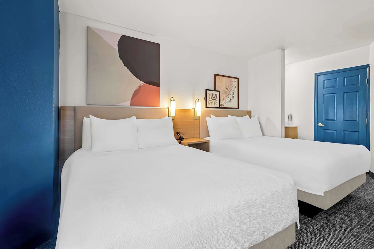 A hotel room with two beds, a blue door, and artwork on the walls.