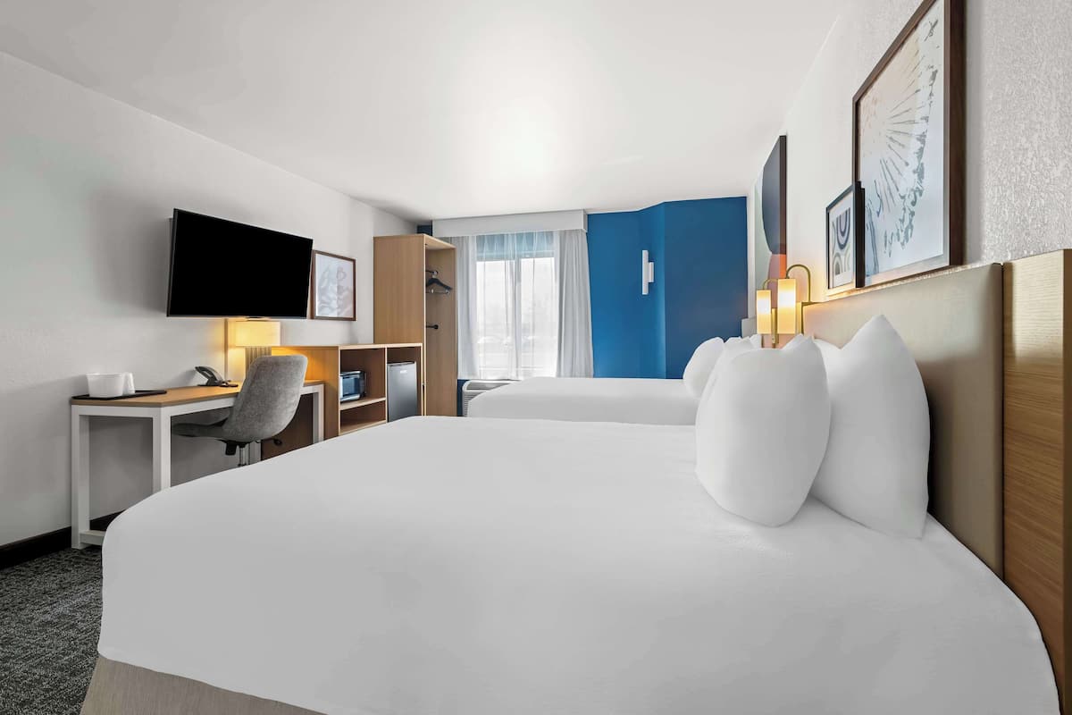 A hotel room with a large bed, a desk with a chair, a flat-screen TV, and a wardrobe.