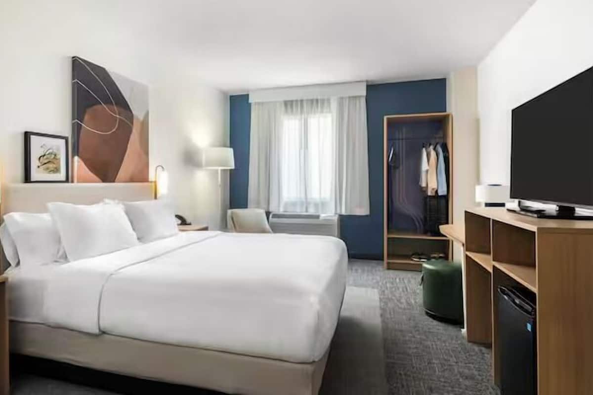 A hotel room with a large bed, bedside tables, a wardrobe, a television, and a window with curtains.