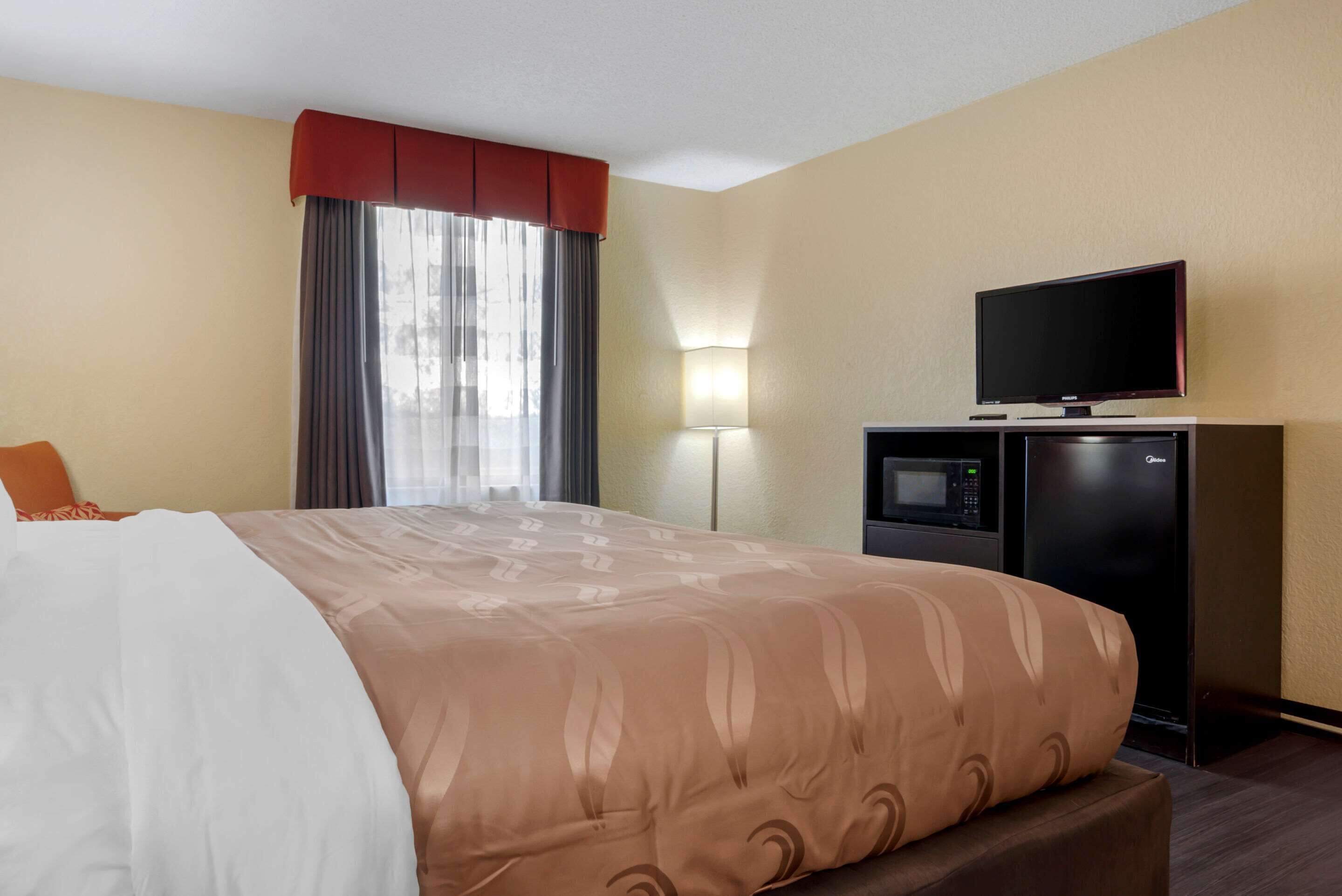 A hotel room with a bed, a television, a microwave, and a desk.