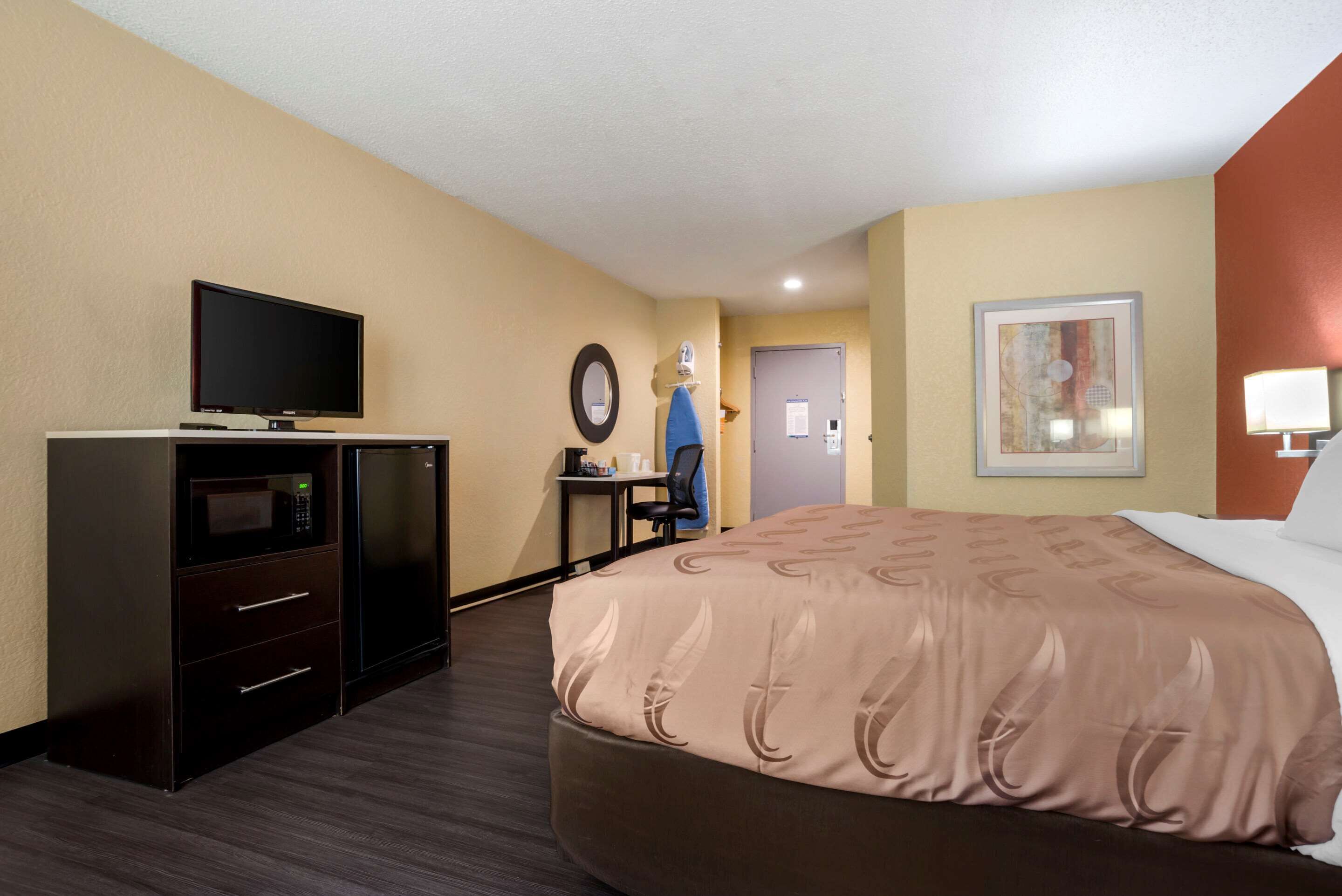 Una habitación de hotel con una cama, televisión, escritorio con silla, microondas y refrigerador.