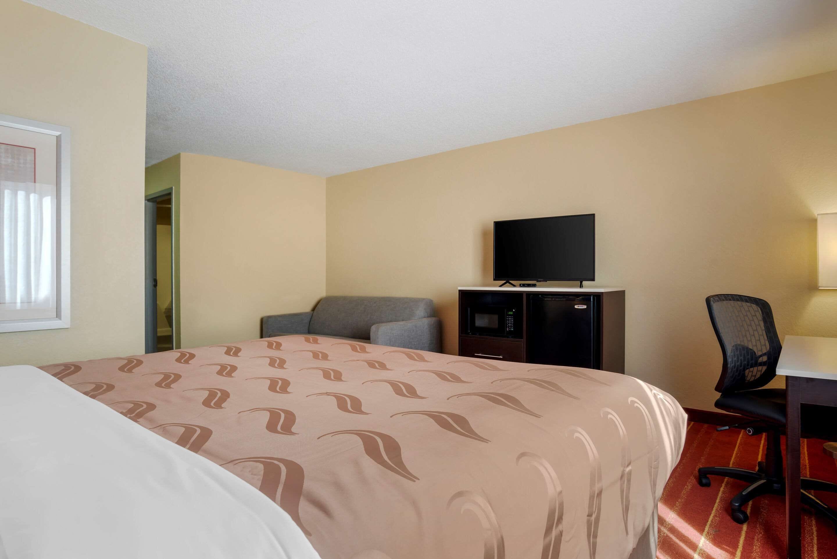 A hotel room with a bed, a desk, a chair, a television, and a minibar.