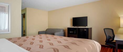 A hotel room with a bed, a desk, a chair, a television, and a minibar.
