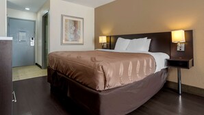 Habitación de hotel con una cama grande, dos lámparas de noche, una puerta a un pasillo y un cuadro en la pared.