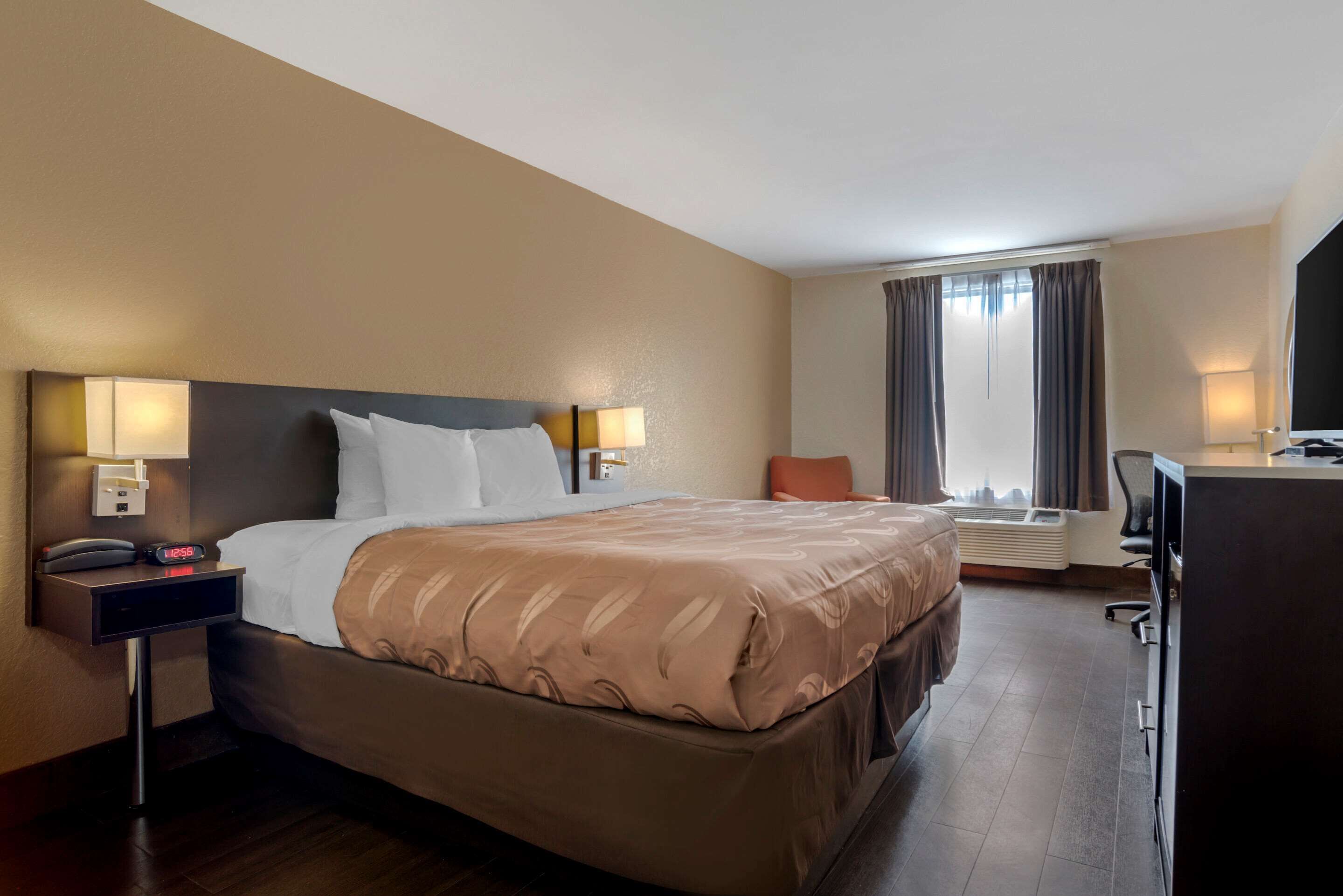 Una habitación de hotel con una cama grande, lámparas de noche, un escritorio y una silla.
