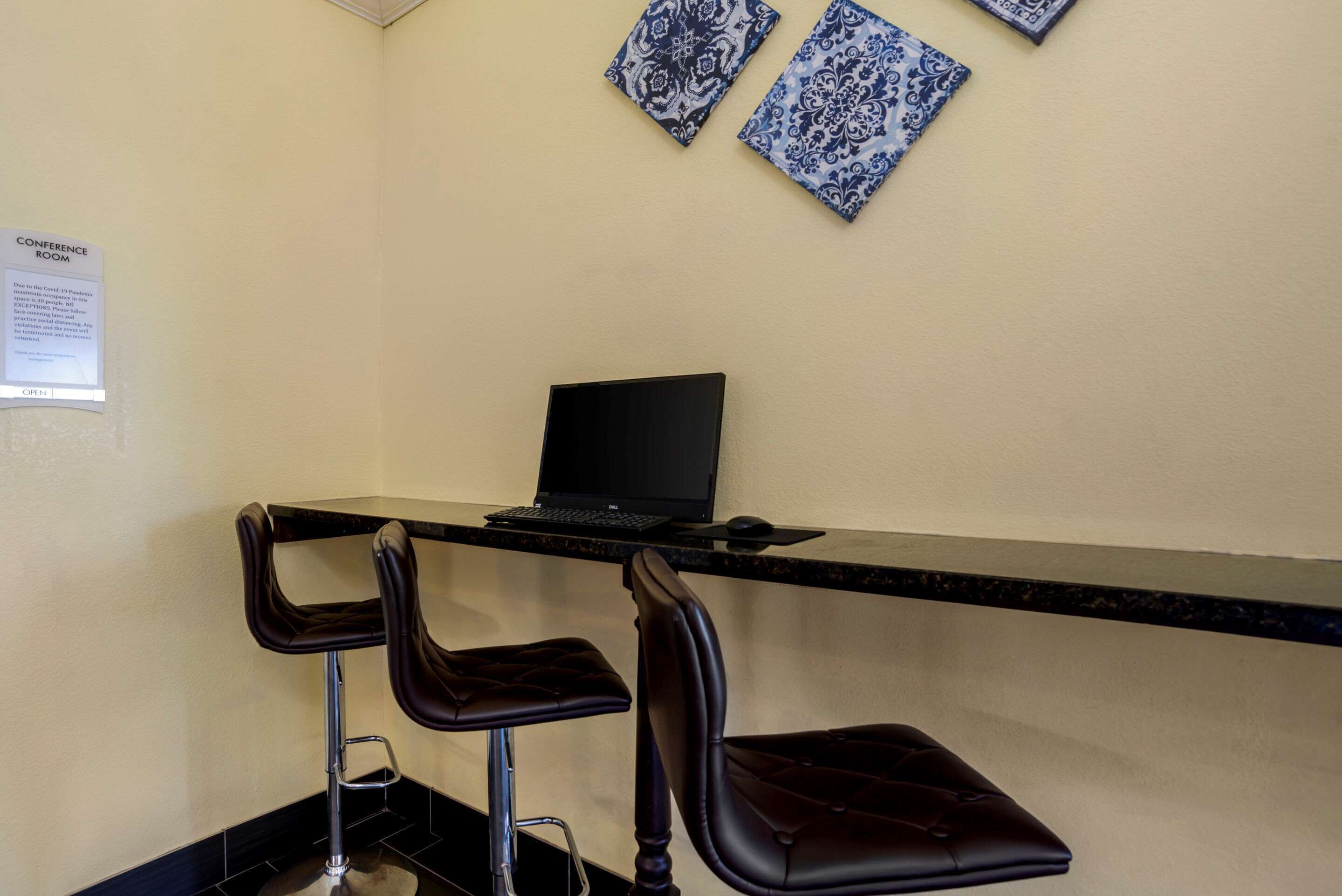 A conference room with a black desk, two bar stools, and a laptop.