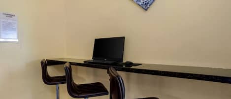 A conference room with a black desk, two bar stools, and a laptop.