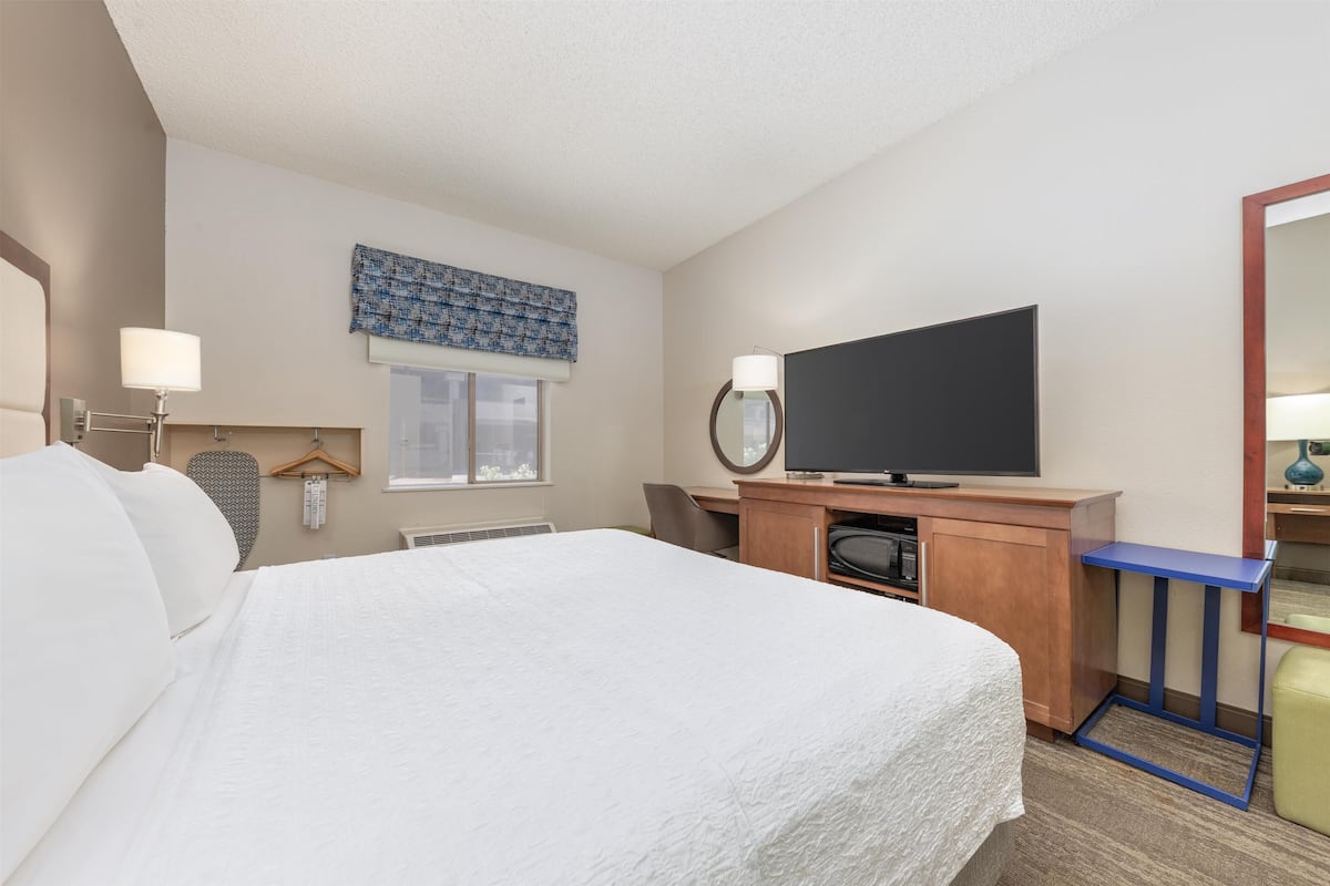 A hotel room with a large bed, a desk with a computer, a flat-screen TV, and a mirror.