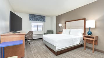 A hotel room with a bed, desk, chair, TV, and bedside lamp.