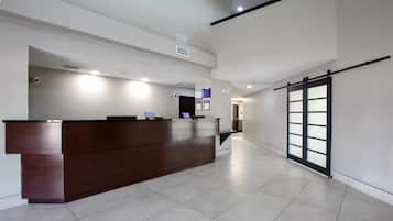 Una moderna zona de recepción con un mostrador de madera, una pantalla digital y un puerta corredera de vidrio que da a otra habitación.