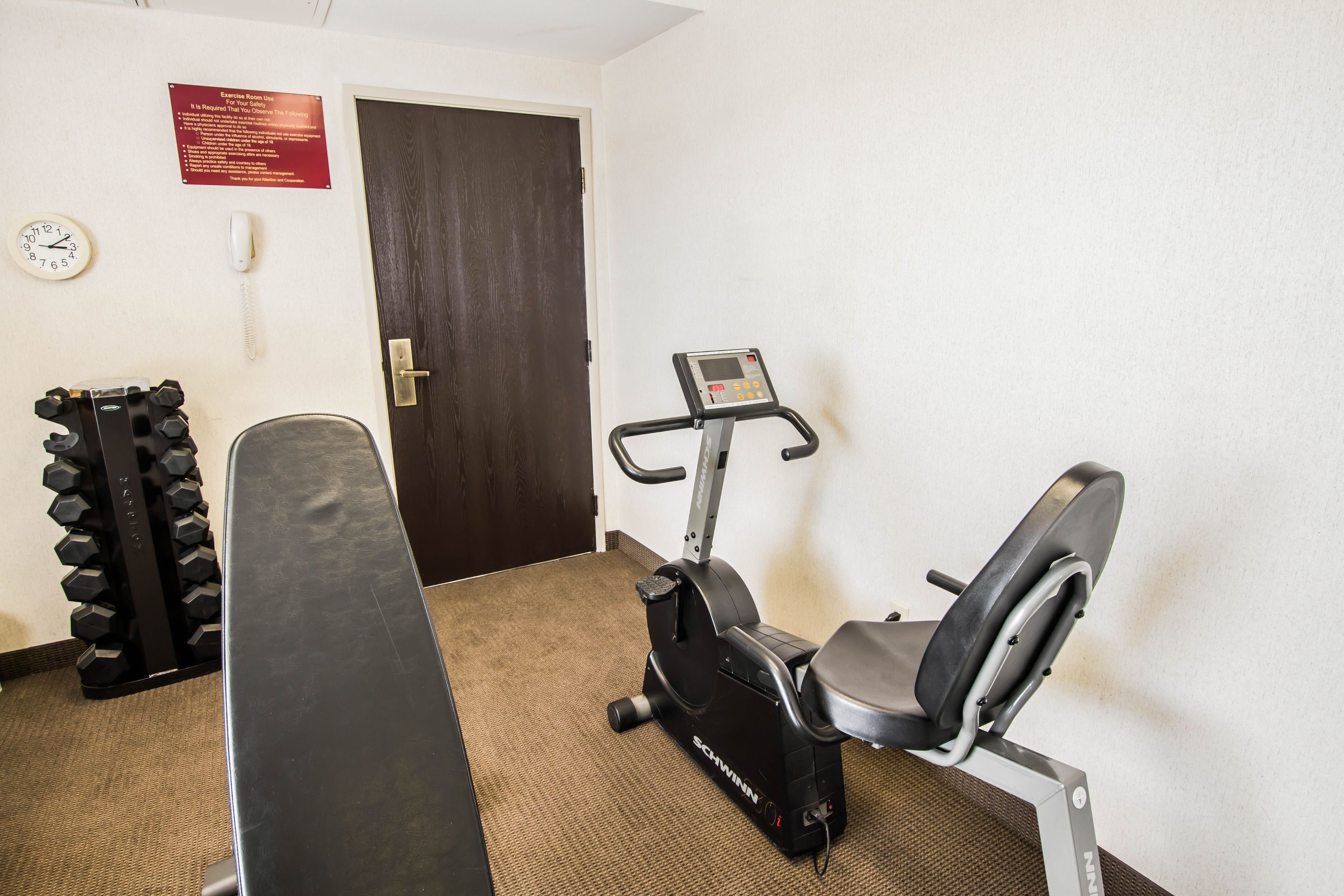 A fitness room with a stationary bike, a bench, and a set of dumbbells.