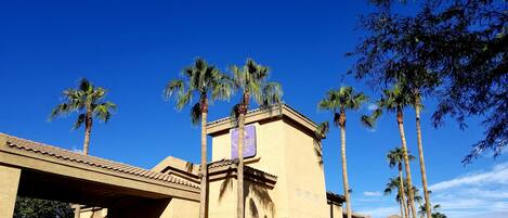 A hotel with a traditional architectural style, featuring a prominent entrance with a tiled roof and palm trees.