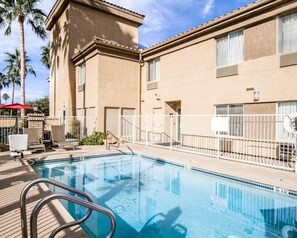 A swimming pool with a metal ladder, surrounded by a white fence, and adjacent to a building with a beige facade and windows.
