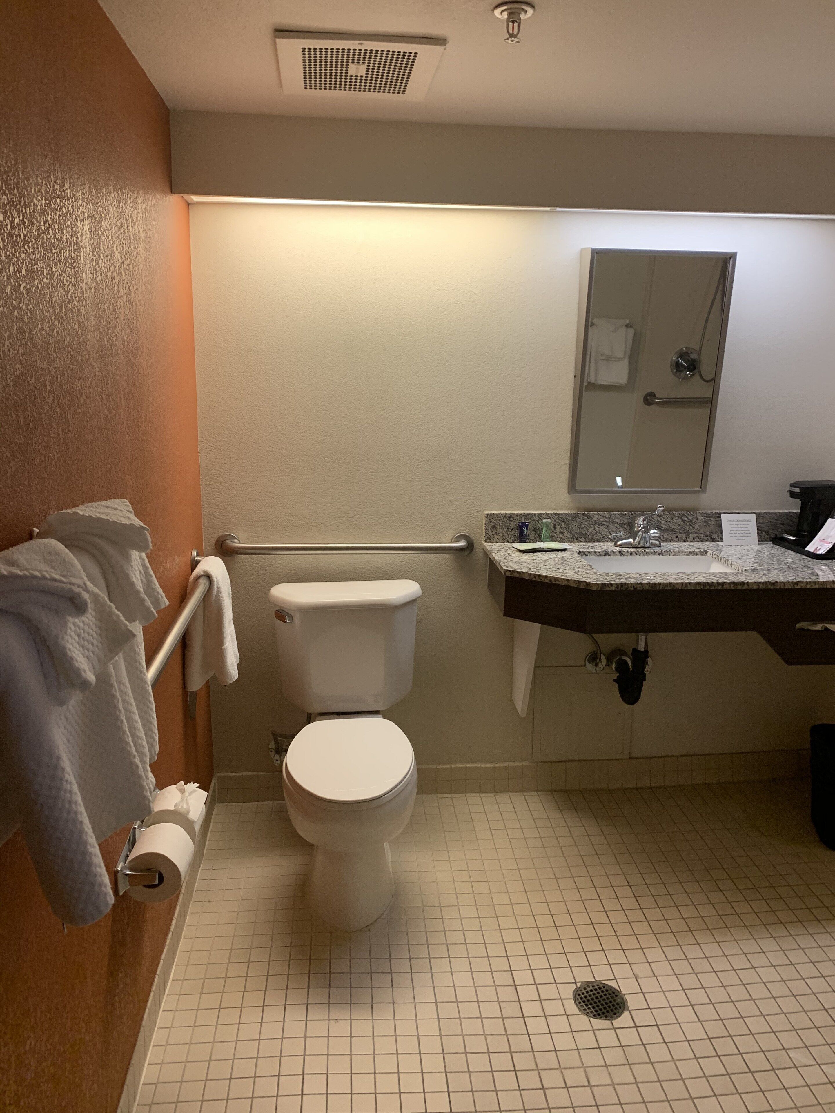 Un baño de hotel estándar con inodoro, lavamanos y espejo.