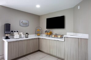 Une cuisine moderne équipée d’un bar pour prendre le petit-déjeuner, d’une machine à café et d’un téléviseur fixé au mur.