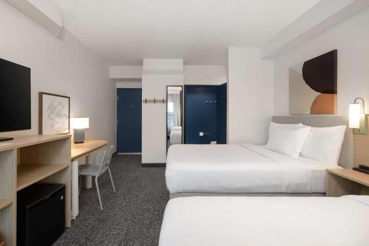 A hotel room with a bed, desk, chair, and a TV.