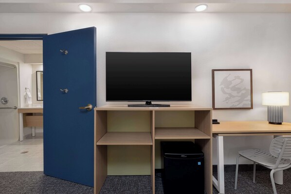 Una habitación de hotel con escritorio, televisión, lámpara y una silla.