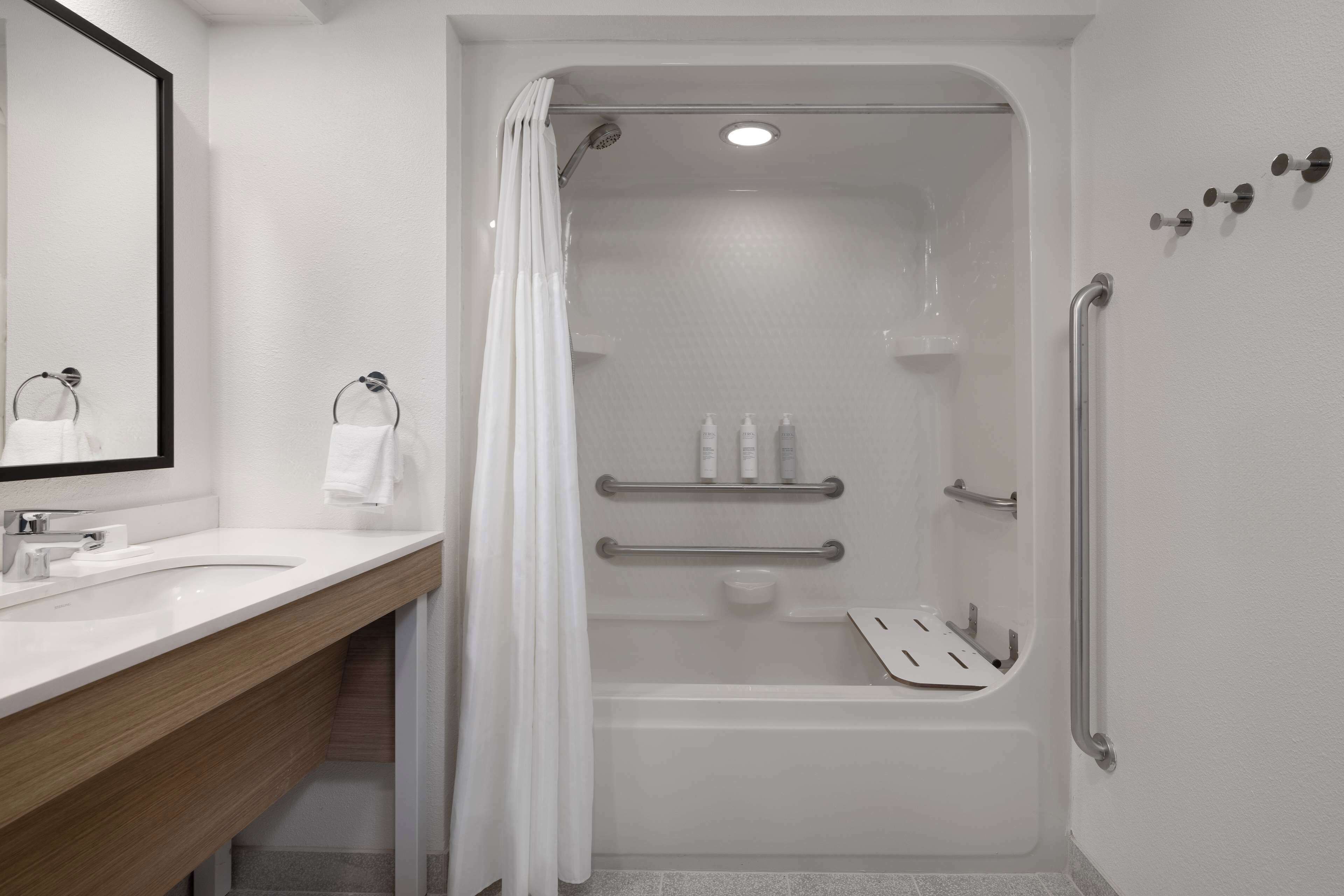 A modern bathroom with a shower, grab bars, and a vanity with a mirror.