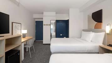 Et hotelværelse med to senge, et skrivebord, en stol, et fjernsyn og et spejl.