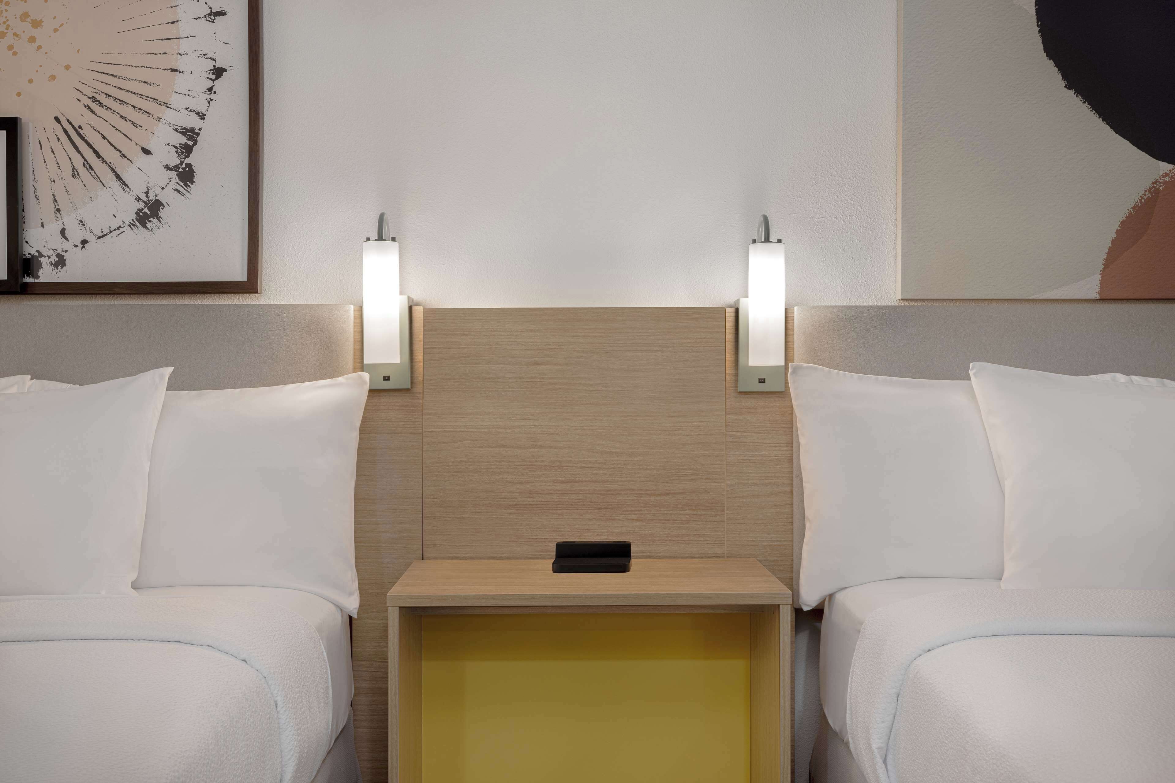 A hotel room with two beds, a wooden headboard, bedside lamps, and a small bedside table.
