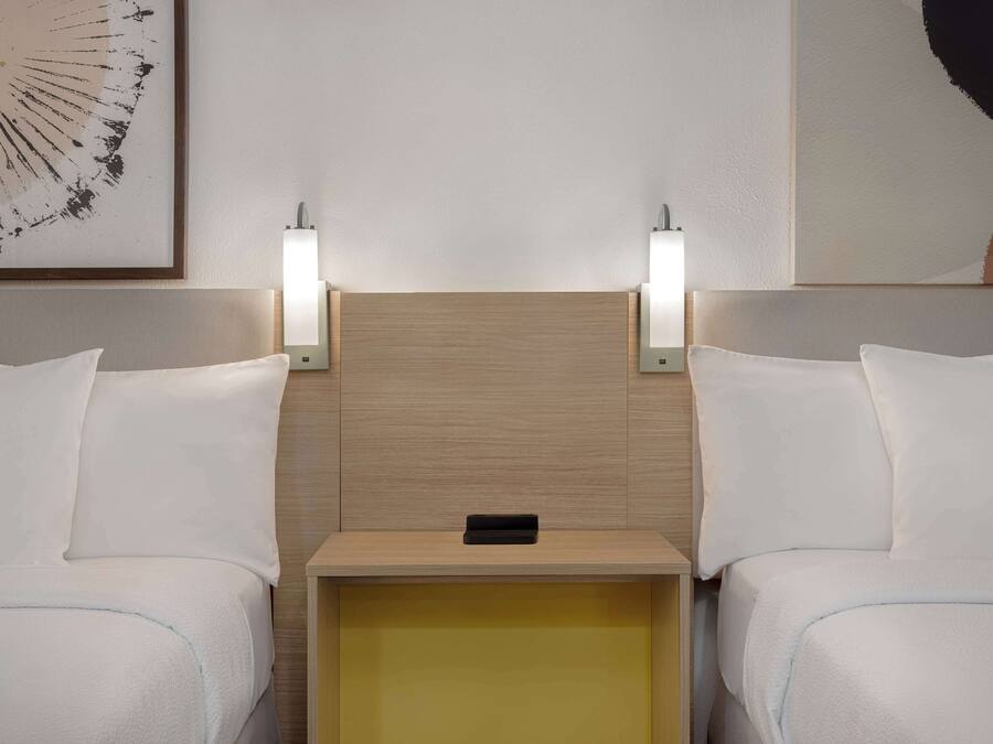 A hotel room with two beds, a wooden headboard, bedside lamps, and a small bedside table.