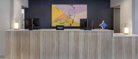 A reception desk with a modern design, featuring a wood-textured surface and a large abstract artwork above.