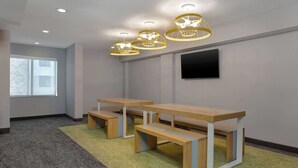 A conference room with three wooden tables and benches, recessed ceiling lights, and a flat-screen TV mounted on the wall. - Spark by Hilton Bentonville (Bentonville)
