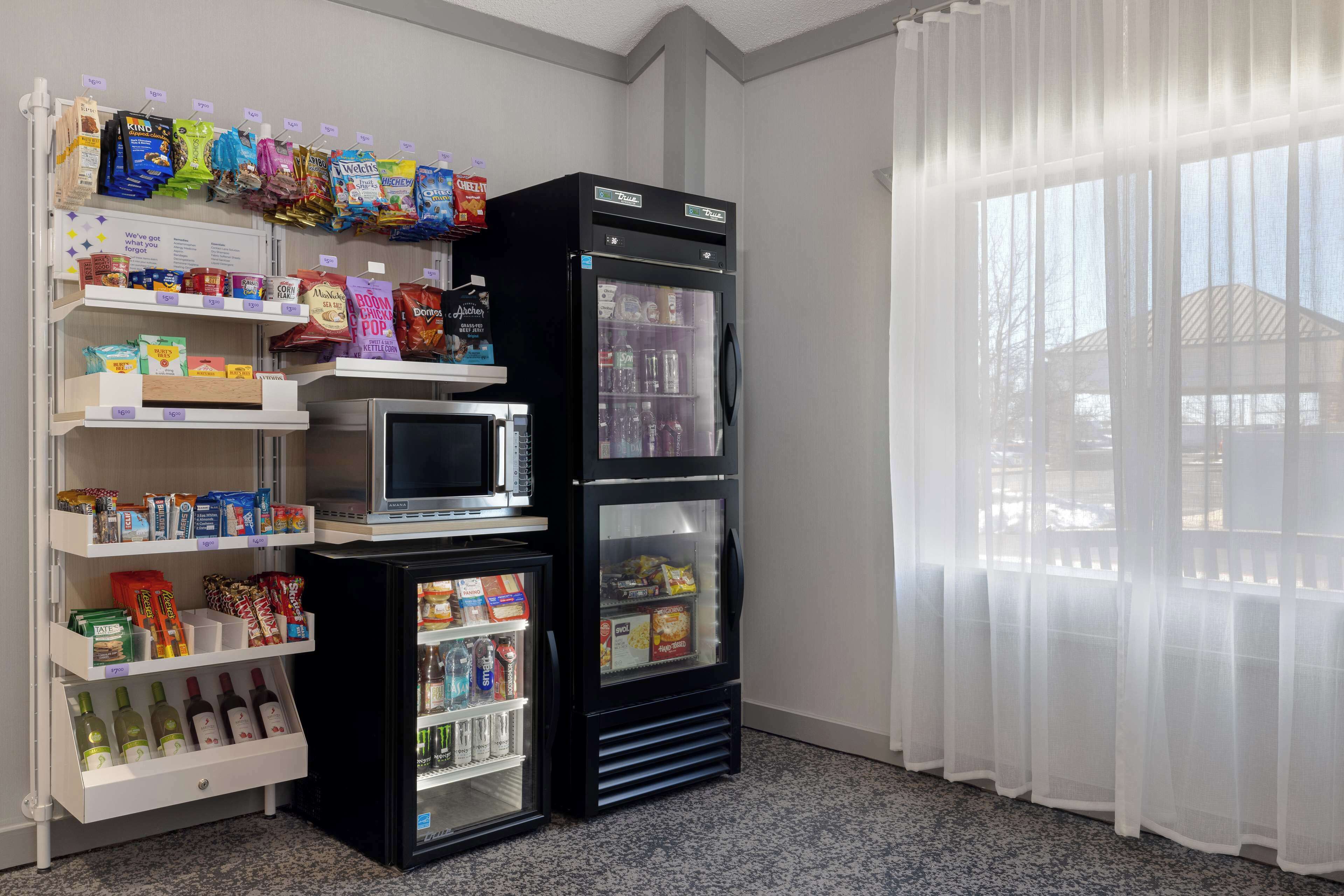 A kitchenette with a microwave, a refrigerator, and shelves stocked with snacks and beverages.