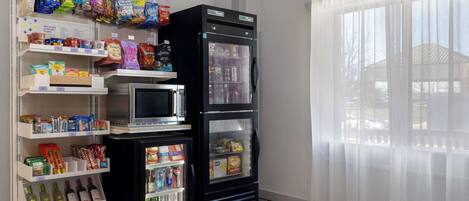 Una kitchenette equipada con microondas, refrigerador y estantes llenos de aperitivos y bebidas.