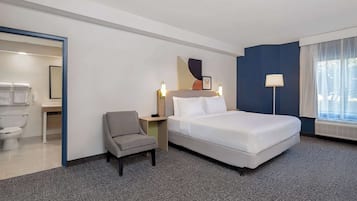 A hotel room with a bed, a chair, a nightstand, a lamp, and a window with curtains.