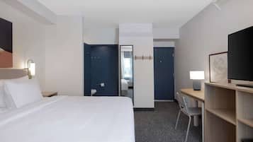 Ein Hotelzimmer mit einem Bett, einem Schreibtisch, einem Sessel, einem Fernseher und einem Spiegel.