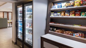 Un bar de aperitivos en un hotel, con un refrigerador lleno de bebidas y una estantería con diferentes marcas de snacks.