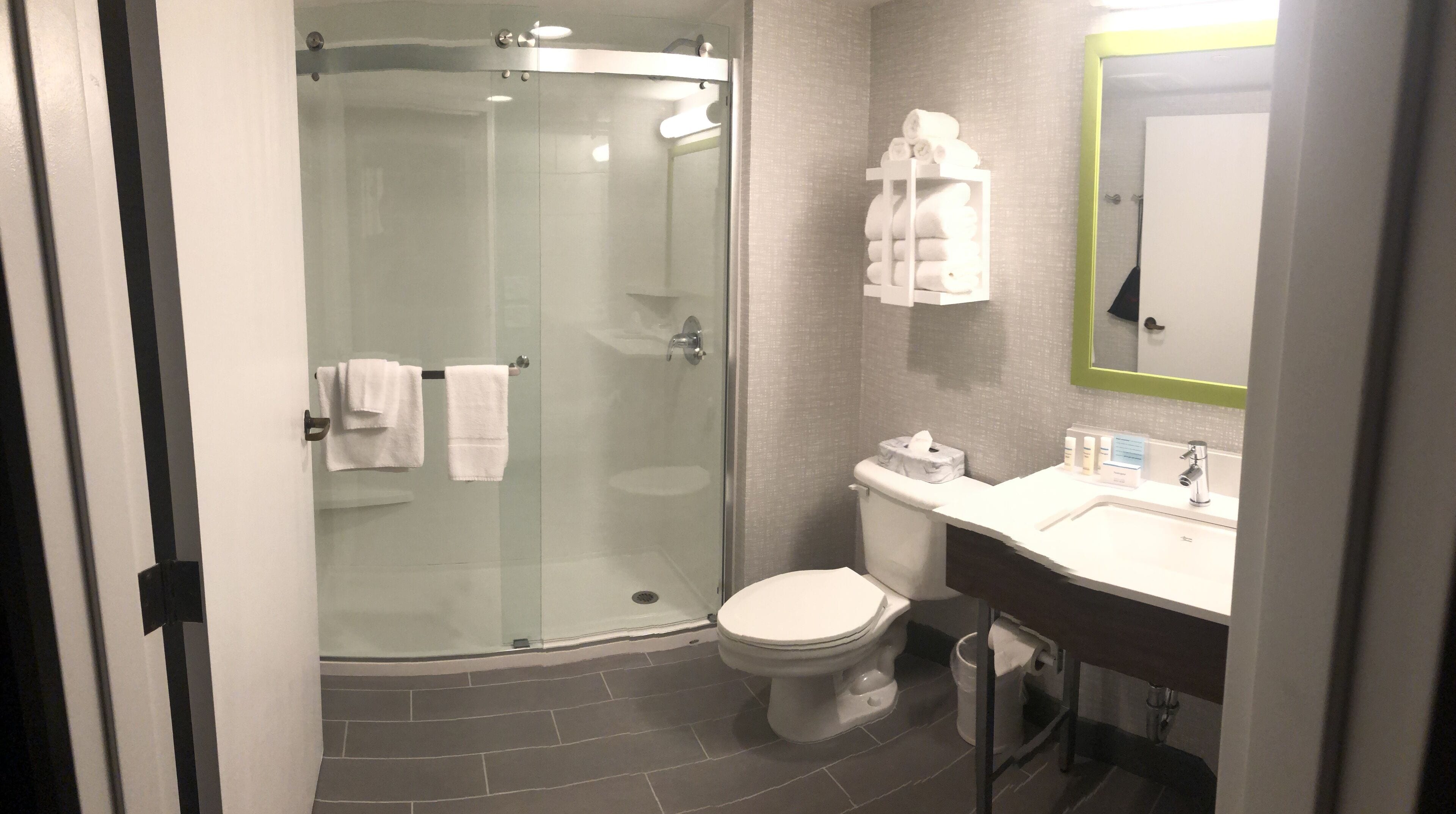 A modern bathroom with a glass-enclosed shower, a toilet, and a sink with toiletries.